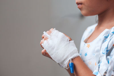 Midsection of patient with bandage wrapped on hand against wall in hospital