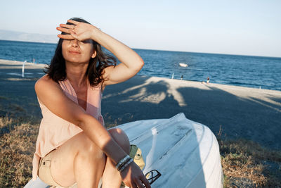 Young woman sitting on the boat at the beach closing her eyes with her hand from the sun. summertime