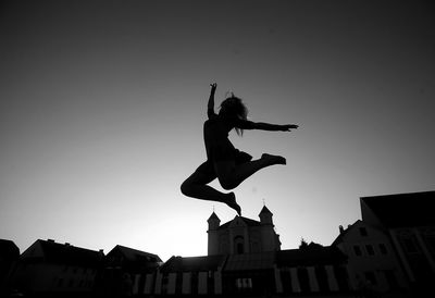 Low angle view of silhouette man jumping against buildings in city