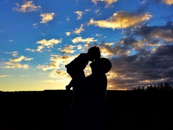 Silhouette couple photographing against sky during sunset