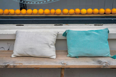 Cushions on wooden bench by oranges arranged at window sill