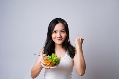 Portrait of young woman holding ice cream against white background