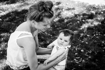 Side view of mother holding daughter while sitting on field