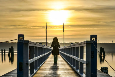 Silhouette woman standing on footbridge against sky during sunset