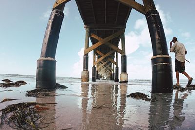 Rear view of man walking below pier on shore