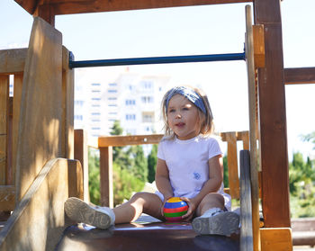 Girl looking away while sitting on wood