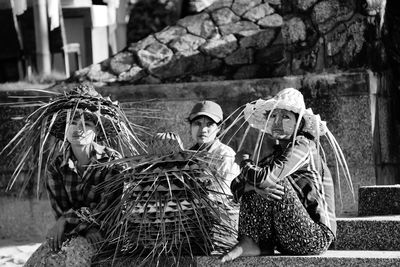 Women sitting on steps with stack of palm leaf hats