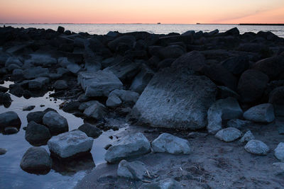 Rocks on beach against sky during sunset