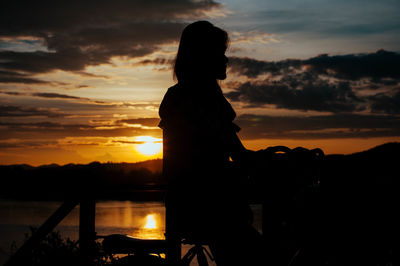 Silhouette woman standing against orange sky during sunset