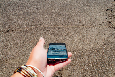 Cropped hand holding mobile phone at beach