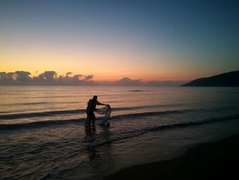 Silhouette people on beach against sky during sunset