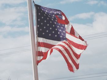 Low angle view of torn american flag against sky