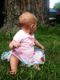 Close-up of baby girls on tree trunk on grassy field