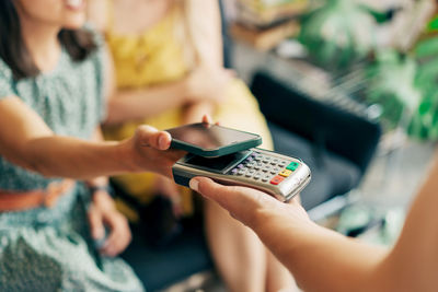 Close up view at hand hold mobile phone, touch a credit card reader inside the coffee shop. cashless