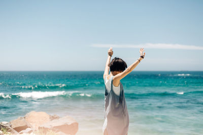 Woman with arms raised standing at beach against sky