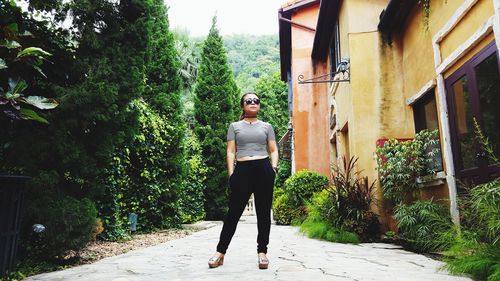 Full length of confident woman in sunglasses standing against trees