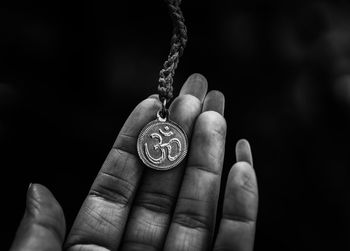 Cropped hand holding om symbol necklace against black background