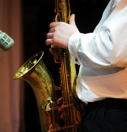 Midsection of male musician playing saxophone by microphone