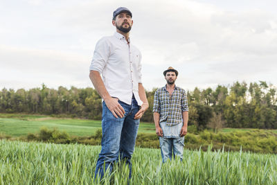 Portrait of male farm workers standing on agricultural field against sky during sunset