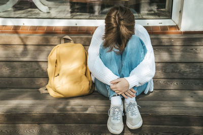 Teenage schoolgirl sitting on a bench hiding her face in her knees, autumn depression