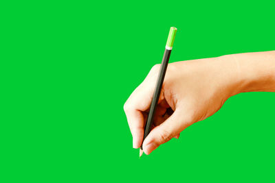 Close-up of hand holding cigarette over green background