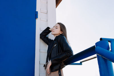 Young woman looking away against wall against clear blue sky