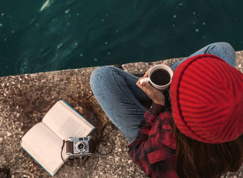 Directly above shot of woman with coffee sitting on pier by lake against sky