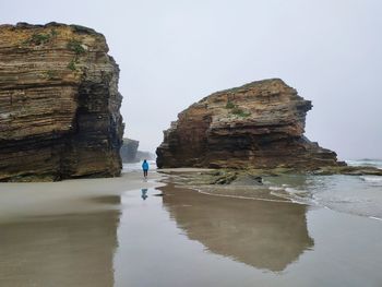 Man standing on rock by sea against sky