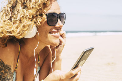 Smiling woman listening music while lying at beach during summer