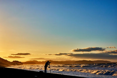 Scenic view of sea and standing person against dramatic sky during sunrise