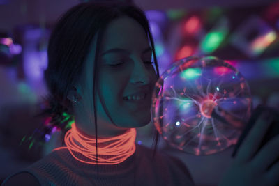 Close-up of smiling woman holding illuminated lighting equipment in room