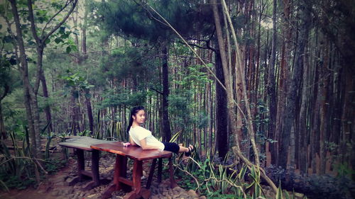 Teenage girl reclining on table against trees in forest