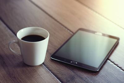 Close-up of coffee cup by digital tablet on table