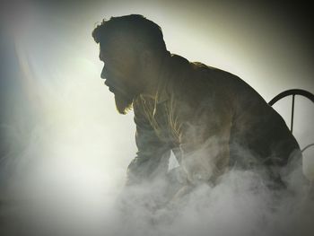 Bearded man sitting amidst smoke in room