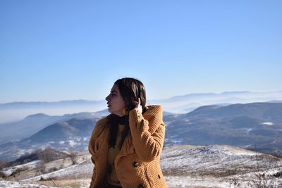Young woman looking away against blue sky at mountains