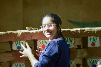 Portrait of young woman standing against fence doing pottery