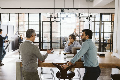 Male and female colleagues looking at mature businessman explaining in creative office