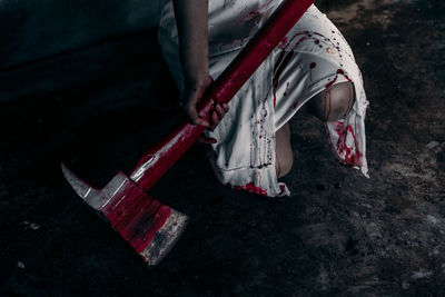 Cropped image of woman wearing dress while holding axe covered with blood