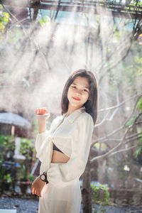 Portrait of young woman standing against trees