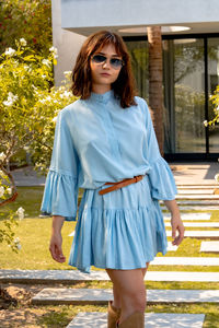 Portrait of young woman standing in a beautiful floral garden, wearing fancy sunglasses.