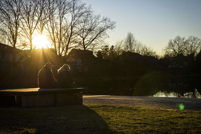 People sitting by lake against sky during sunset