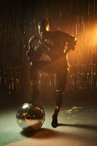 Stylish young african american woman in high heeled boots with hand on hip looking at camera while leaning on glitter ball