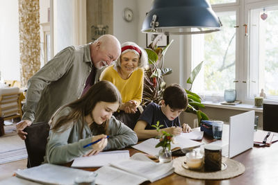 Smiling grandparents with grandchildren studying at home