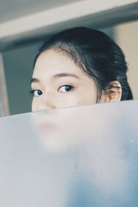 Close-up portrait of young woman hiding behind glass