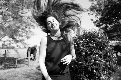 Portrait of smiling woman tossing hair while standing by plant