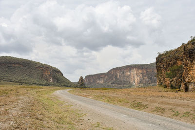 Dirt road amidst mountains against sky