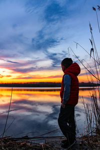 Man standing by lake against sky during sunset