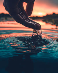 Low section of person in sea against sky during sunset