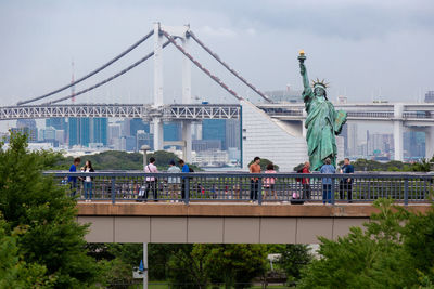 People at bridge against sky in city