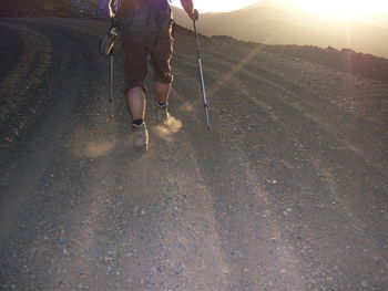 Low section of man standing on road at sunset